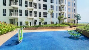 A swimming pool with a blue surface, surrounded by a low wall and greenery. - Good And Cozy Studio At Apartment Tokyo Riverside Pik 2 (Jakarta)