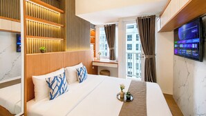 A hotel room with a bed, a desk, a TV, and a view of buildings. - Good And Cozy Studio At Apartment Tokyo Riverside Pik 2 (Jakarta)