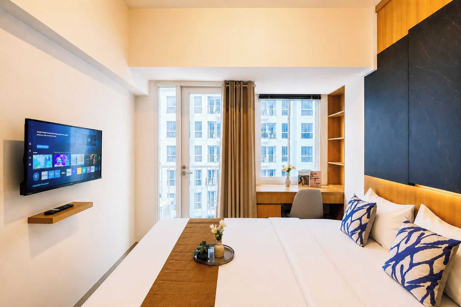 Une chambre d’hôtel avec un lit, un bureau, une télévision et une vue sur les bâtiments par la fenêtre.