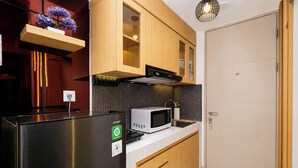 A compact kitchen with a stainless steel refrigerator, a microwave, and wooden cabinets. - Warm Stylish Studio Apartment Tokyo Riverside Pik 2 (Jakarta)
