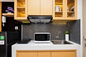Une cuisine moderne dotée d’une hotte Tixx noire, d’un four à micro-ondes blanc, d’un évier en acier inoxydable et de meubles de rangement en bois.