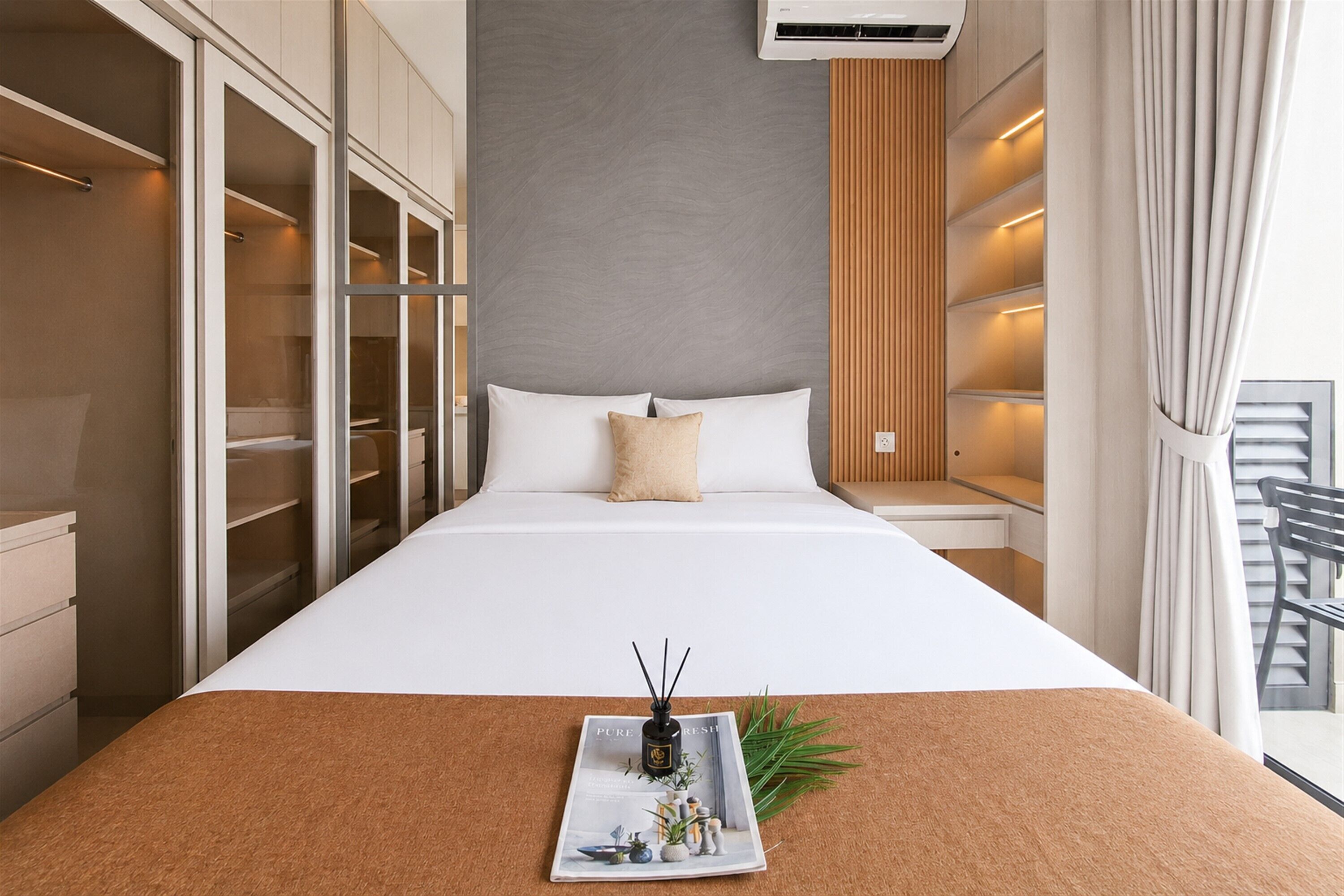 A hotel room with a large bed, a built-in wardrobe, a bedside table, and a window with curtains.