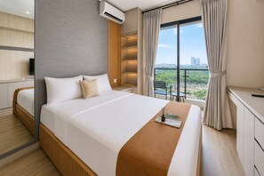 A hotel room with a large bed, a TV, a balcony with a city view, and a desk with a chair. - Comfortable And Modern Studio Room At Apartment Sky House Bsd (Tangerang)