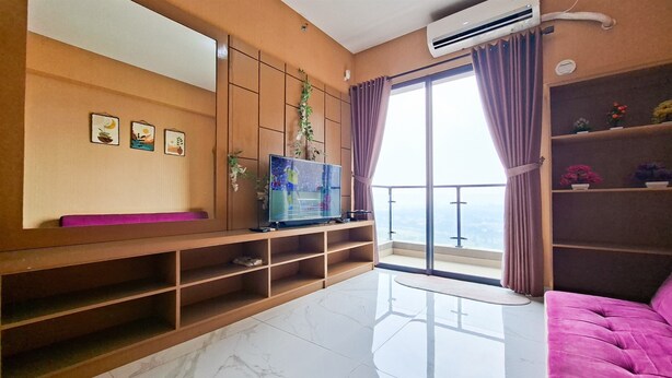 A modern living room with a flat-screen TV, a sofa, a balcony with a view, and a large window with curtains. - Compact And Warm 2Br Apartment Sky House Bsd (Tangerang)