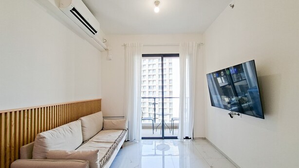 A modern living room with a sofa, a flat-screen TV mounted on the wall, and a large window with curtains. - Modern Comfy 2Br Sky House Bsd Apartment (Tangerang)
