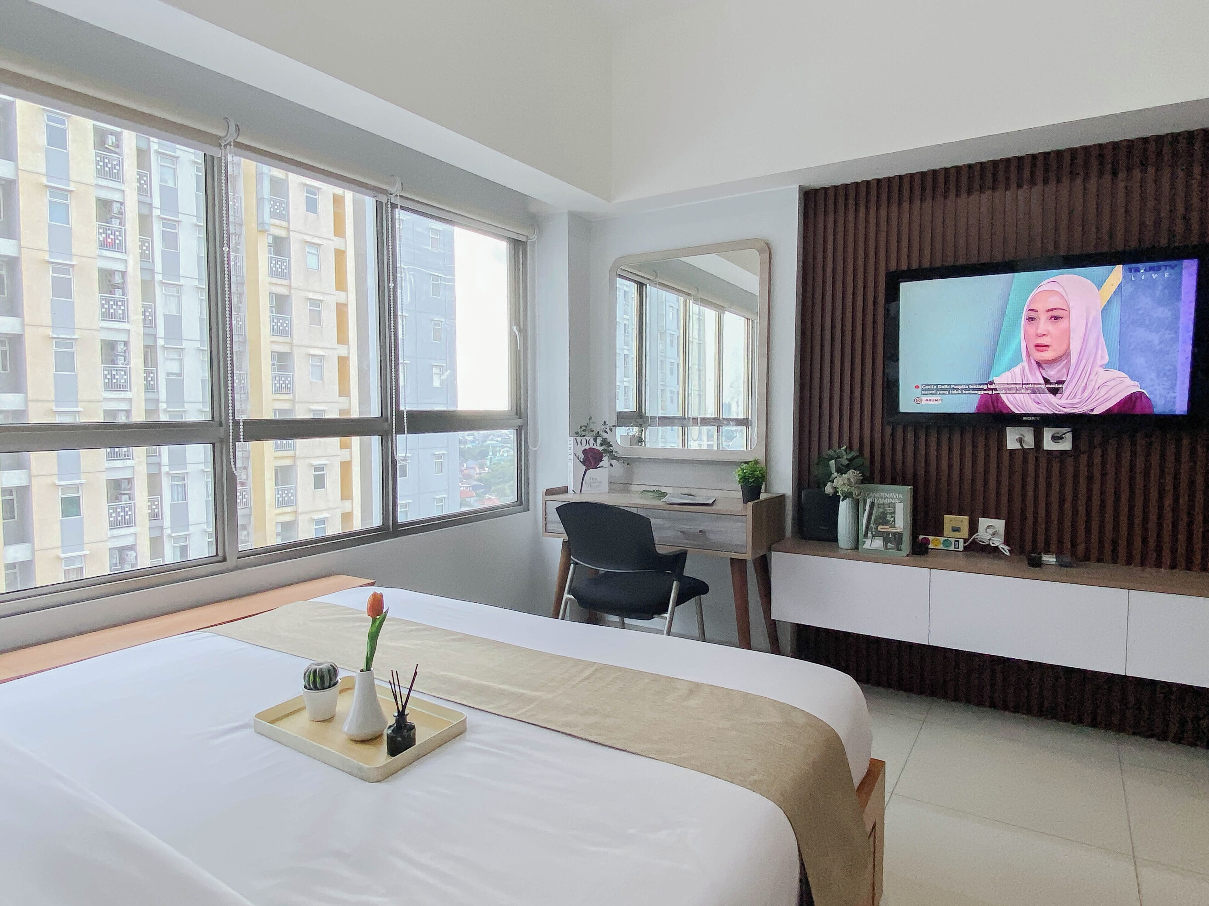 A hotel room with a bed, a desk, a television, and large windows.