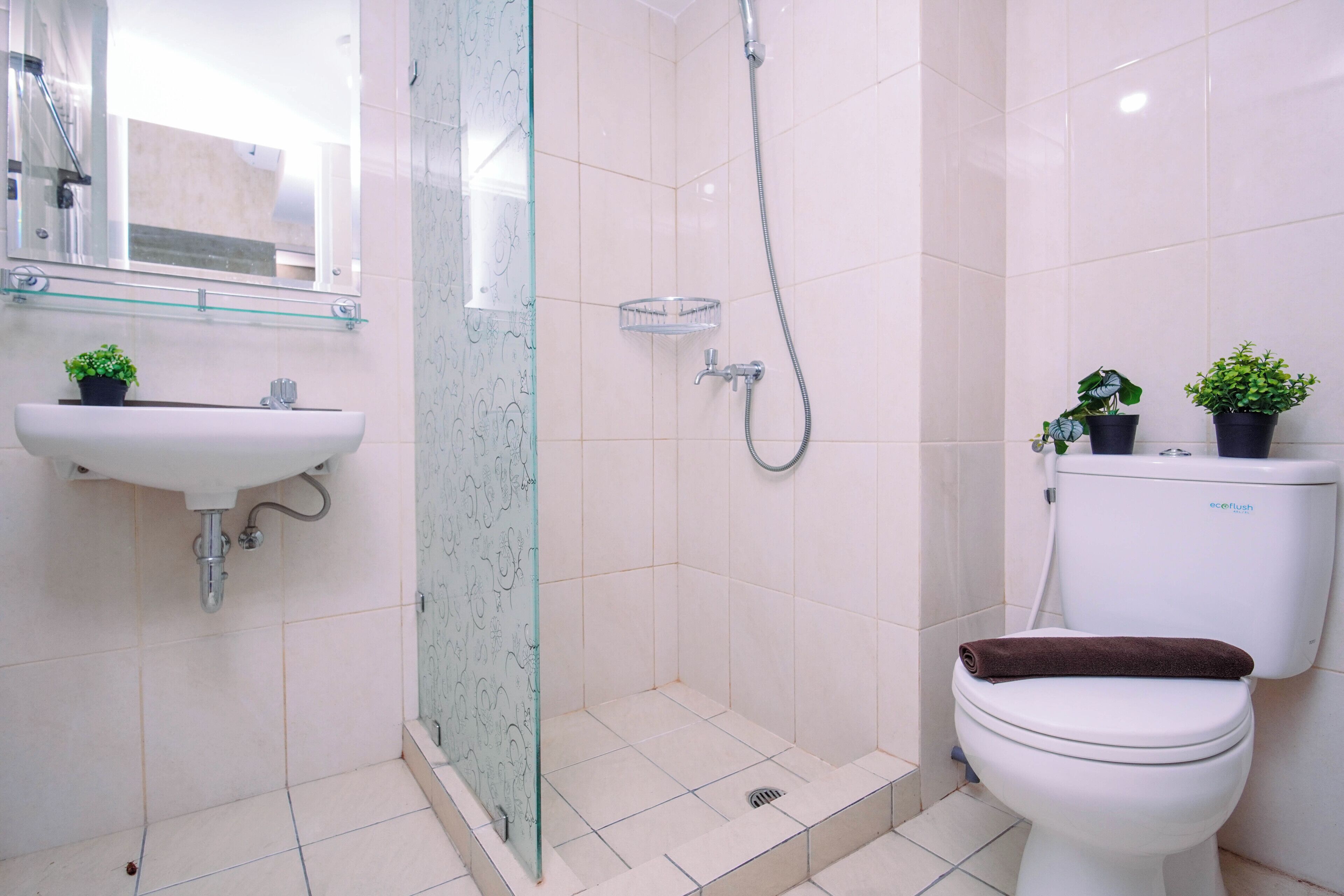 A bathroom with a sink, toilet, shower, and two potted plants.