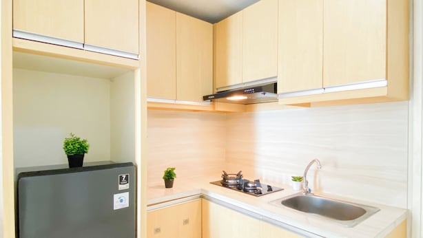 Eine kleine Küche mit Holzschränken, einer Edelstahlspüle und einem schwarzen Kühlschrank.