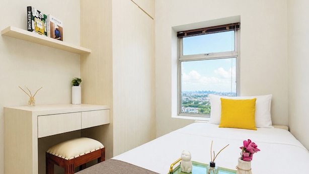 Ein modernes Hotelzimmer mit einem Bett, einem Fenster mit Blick auf die Stadt, einem kleinen Schreibtisch mit Ablagefläche und einem Nachttisch mit Tablett.