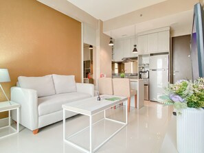 Ein modernes Wohnzimmer mit einem weißen Sofa, einem Couchtisch und einer Küchenzeile inklusive Kühlschrank und Schränken.
