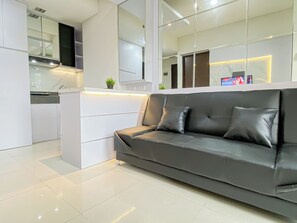 Una sala de estar moderna con un sofá gris, un mueble blanco y una cocina al fondo.