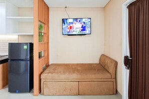 Un espace de vie compact comprenant un canapé, un téléviseur fixé au mur et un réfrigérateur.