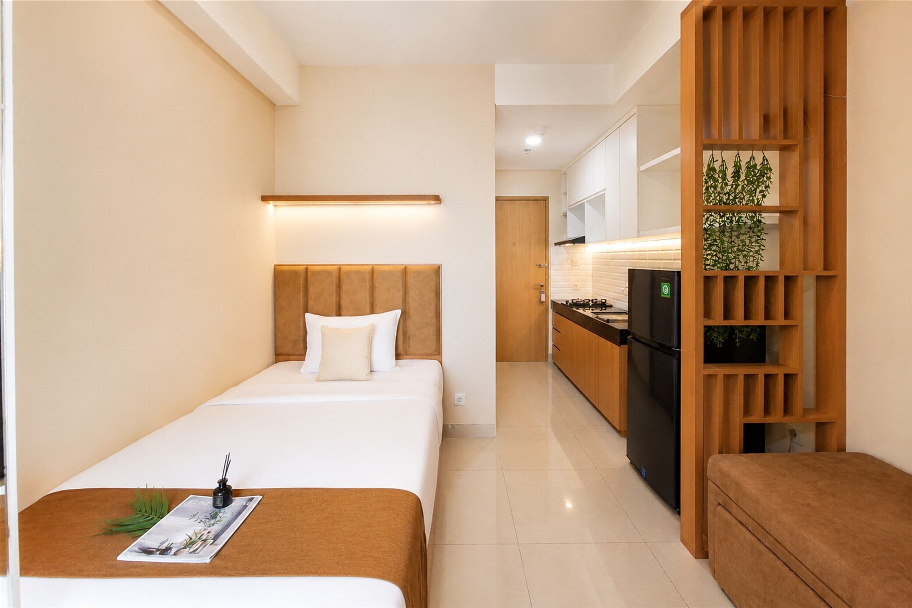 A hotel room with a bed, bedside table, and a kitchenette area.