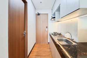 A narrow kitchen with a wooden door, a black countertop, a sink, and a stove. - Cozy And Warm Full Furnished Studio Room At Apartment B Residence (Tangerang)