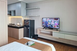 Ein kompaktes Hotelzimmer mit Küchenzeile, Flachbildfernseher, Bett und einer kleinen Sitzecke.