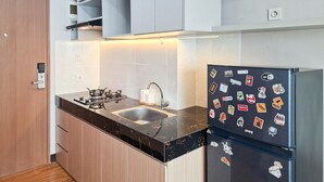 A compact kitchen with a gas stove, a sink, and a refrigerator adorned with various stickers. - Cozy And Warm Full Furnished Studio Room At Apartment B Residence (Tangerang)