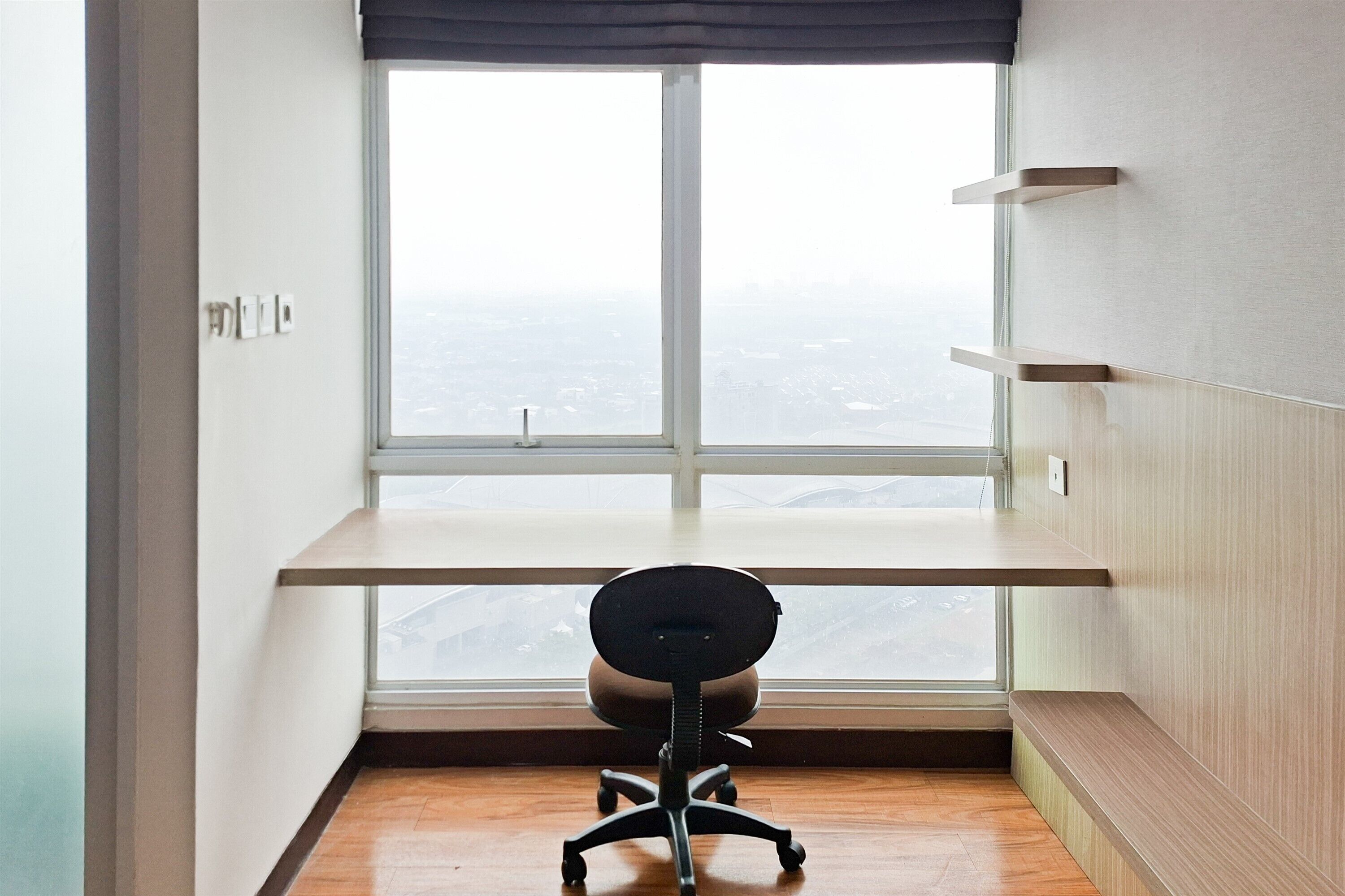 A room with a desk, chair, and a large window with a view of a cityscape.