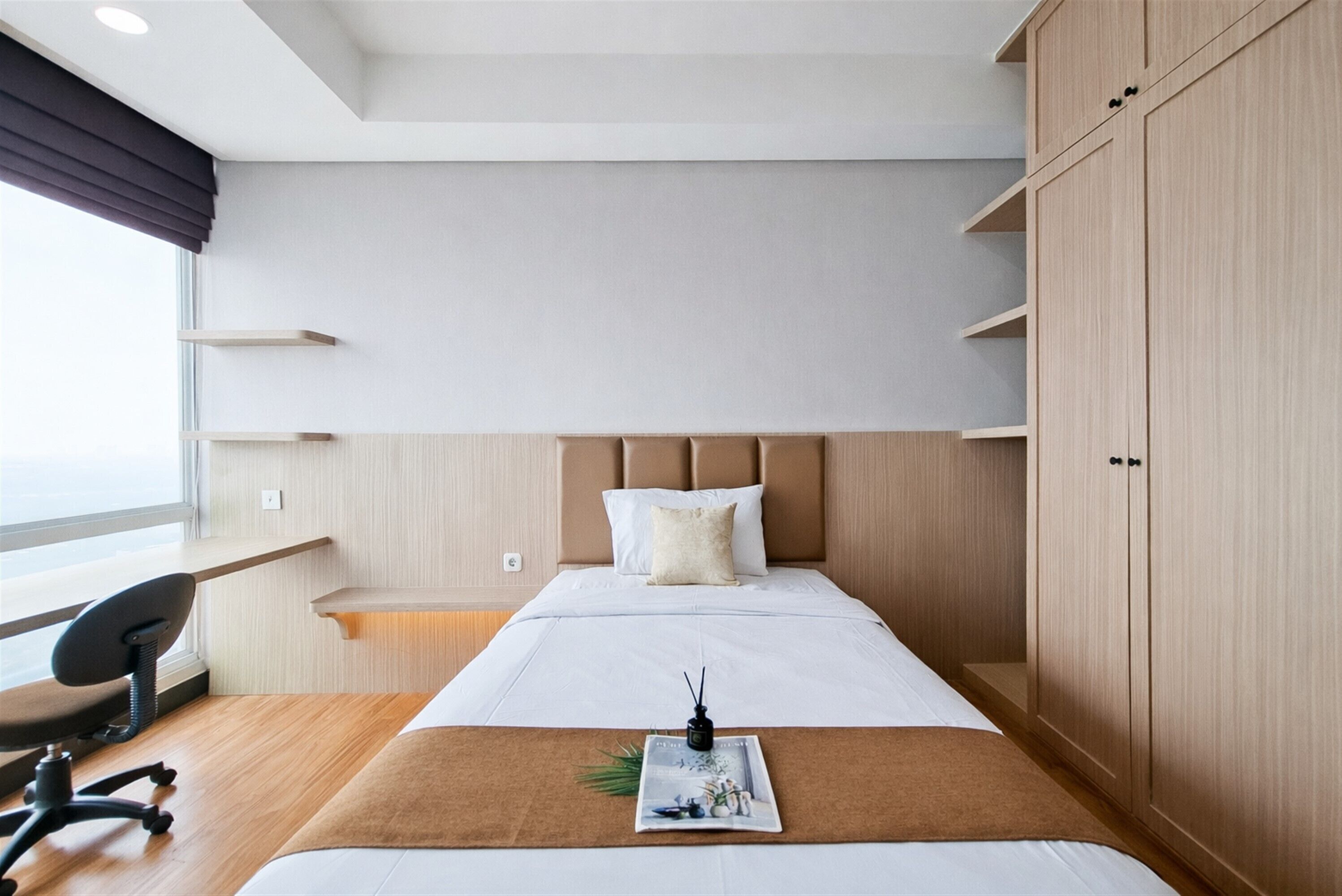 A modern hotel room with a bed, a desk, a chair, and built-in wooden cabinets.