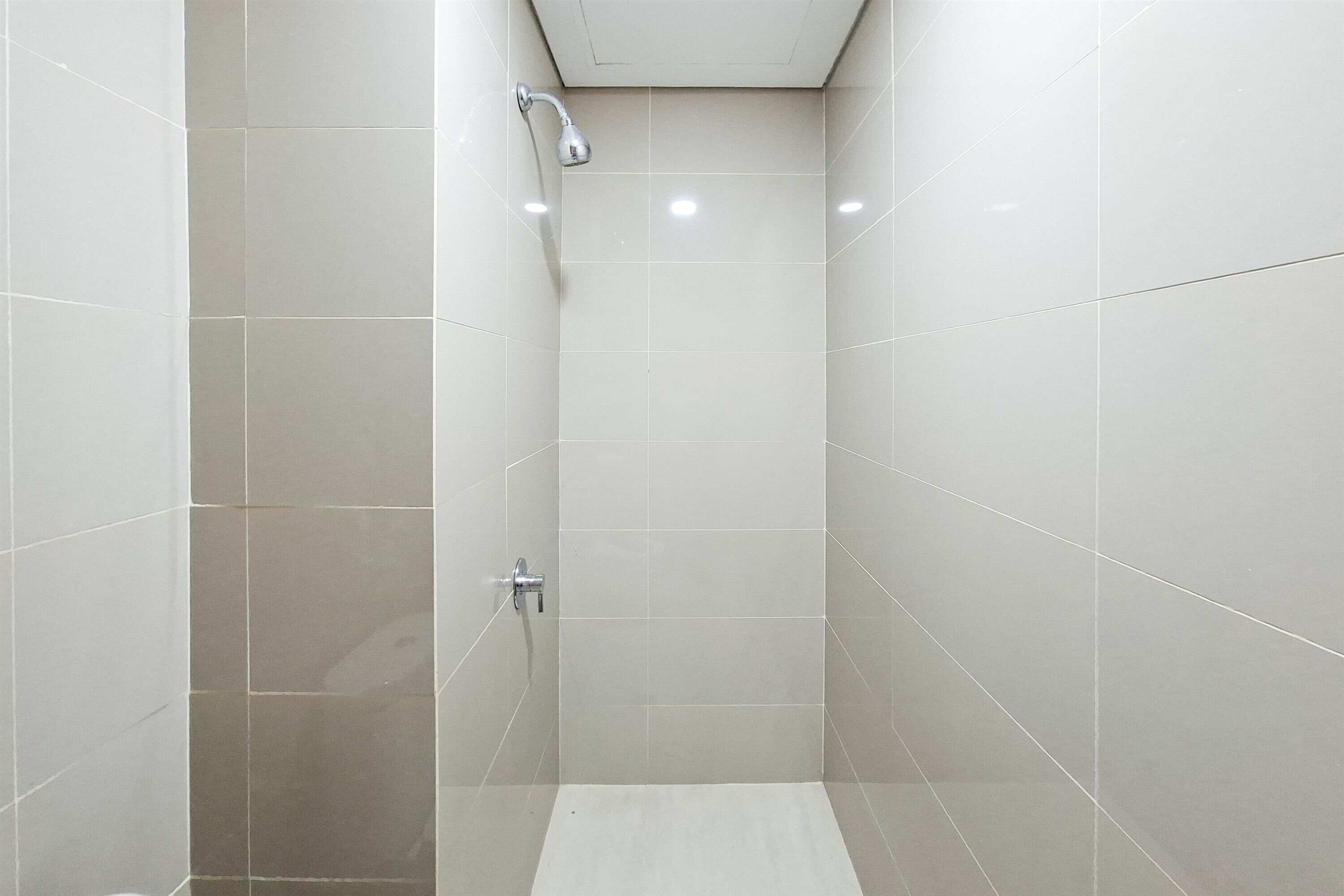 Un vestíbulo de ducha estrecho, con azulejos, con un cabezal de ducha de mano y un grifo instalado en la pared.