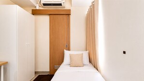 Een compacte, verzorgde slaapkamer met een bed, een kledingkast, een bureau en een airconditioning.