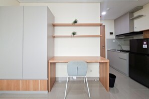 A modern kitchen with a built-in desk, a grey chair, and a small plant on the shelf. - Comfortable And Homey Studio Room At Apartment B Residence (Tangerang)