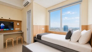 A modern hotel room with a bed, a TV, a desk, and a window with a city view. - Comfortable And Homey Studio Room At Apartment B Residence (Tangerang)