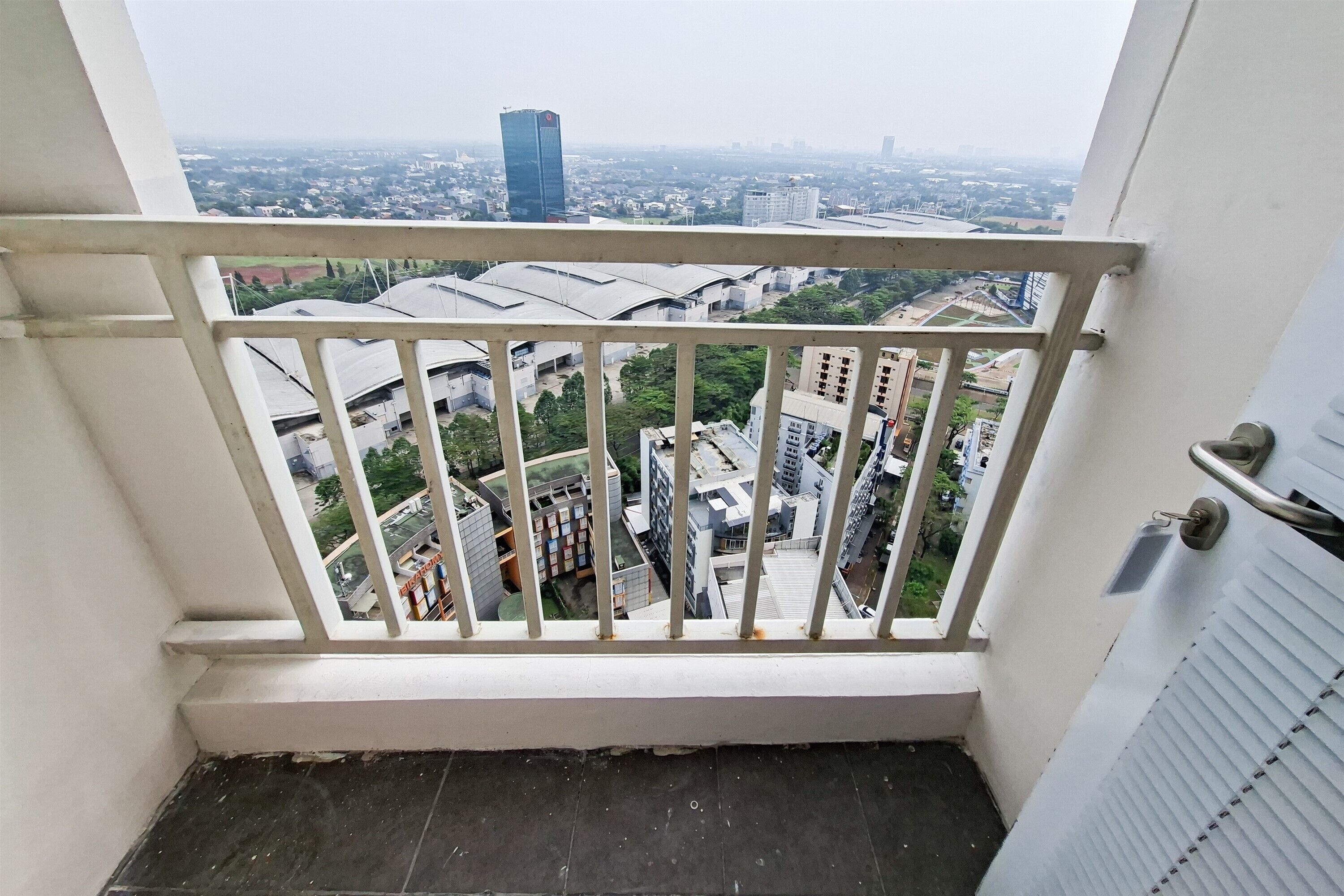 Un balcón con vistas a un paisaje urbano, que incluye un edificio alto y edificios residenciales.