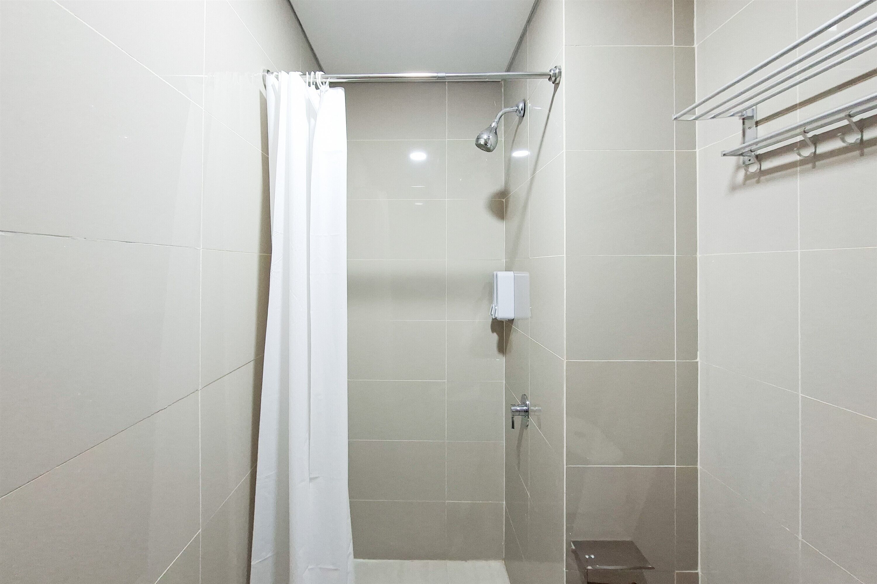 Een douche met een glazen deur, een witte douchegordijn en een handdouche.
