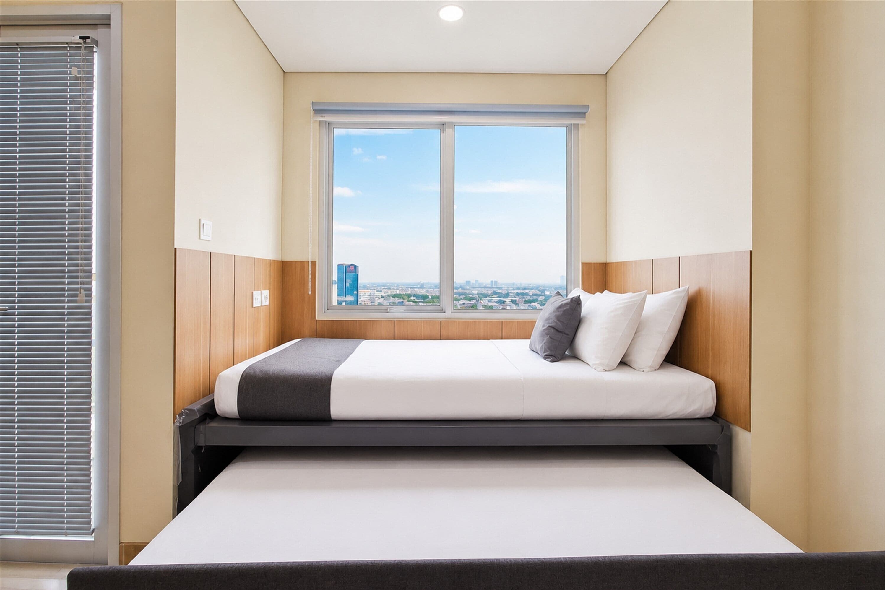 Un dormitorio con cama, ventana y vista a la ciudad.