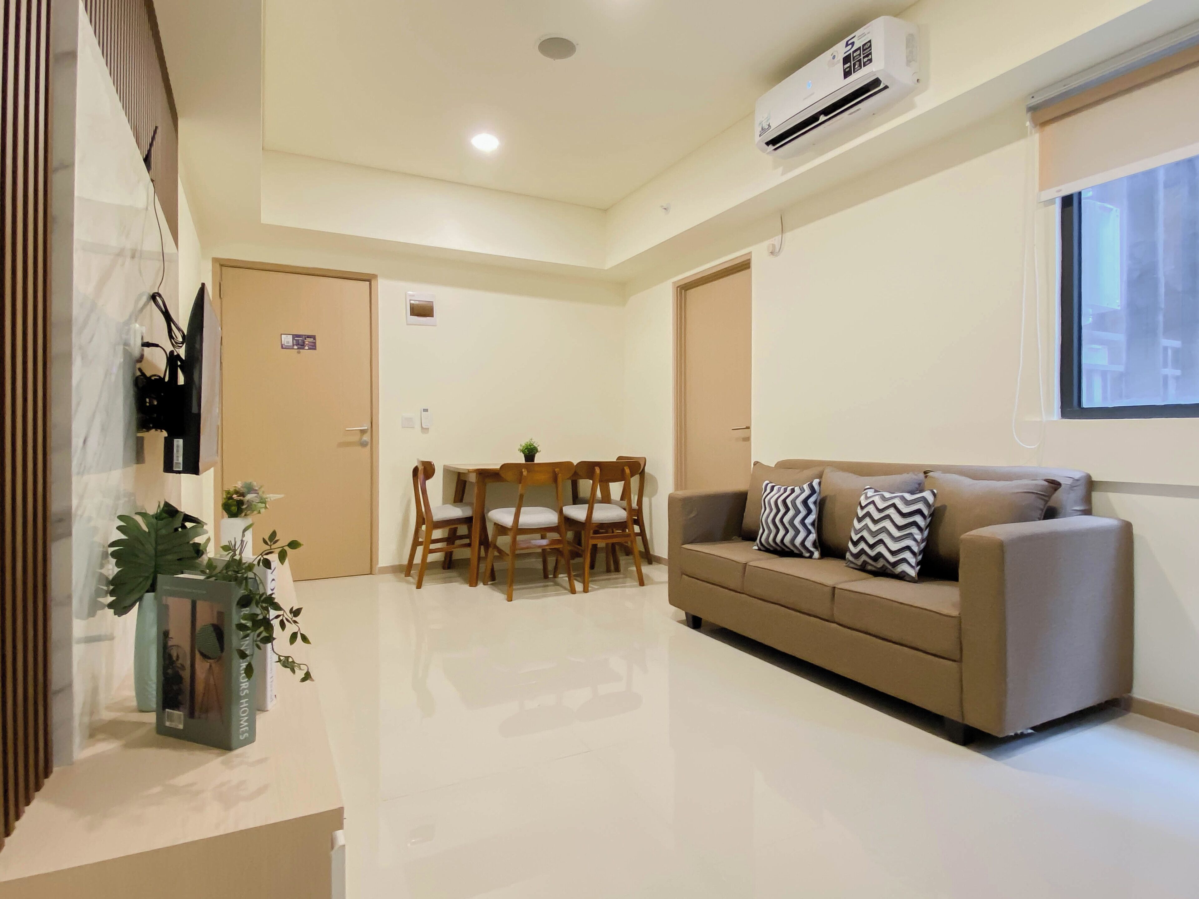 A modern living room with a sofa, a dining table with chairs, and an air conditioning unit on the wall.