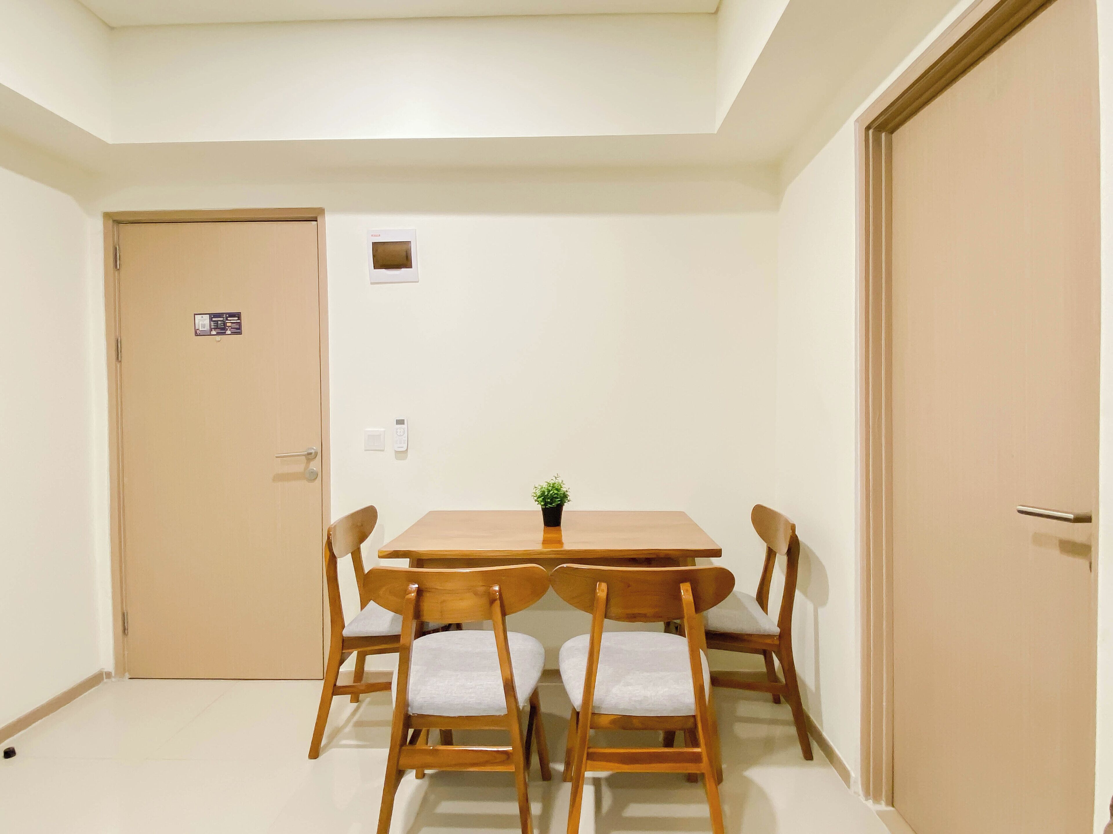 Una habitació amb una taula de dinar de fusta, quatre cadires, una petita planta en test i dues portes.
