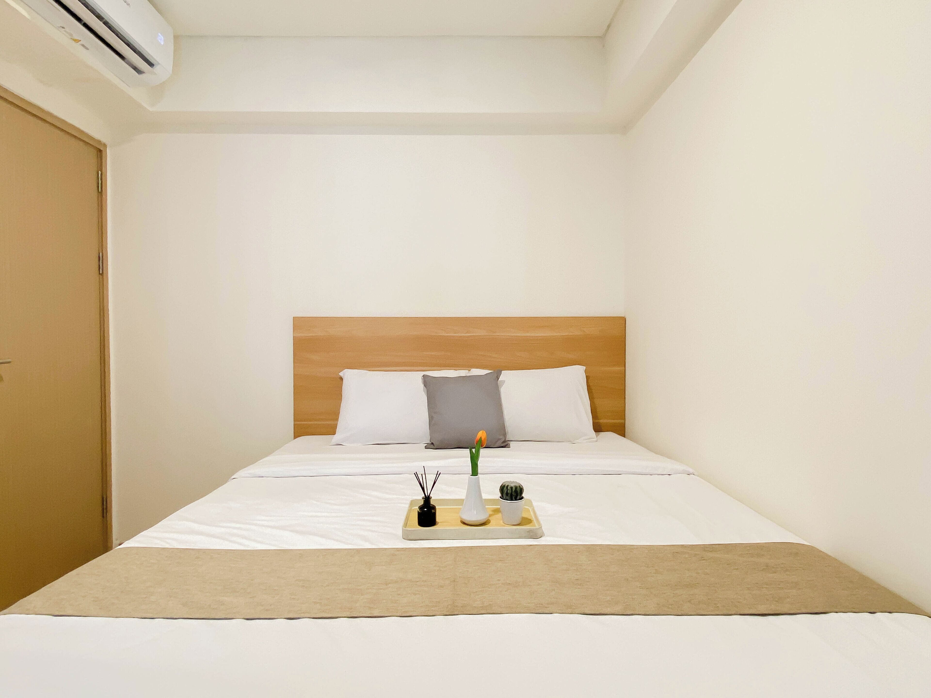 A hotel room with a bed, a wooden headboard, white bedding, a tray with a candle, and a small plant.