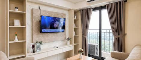Ein modernes Wohnzimmer mit einem an der Wand montierten Flachbildfernseher, einer Sofagarnitur, einem Couchtisch und einem Balkon mit Vorhängen.