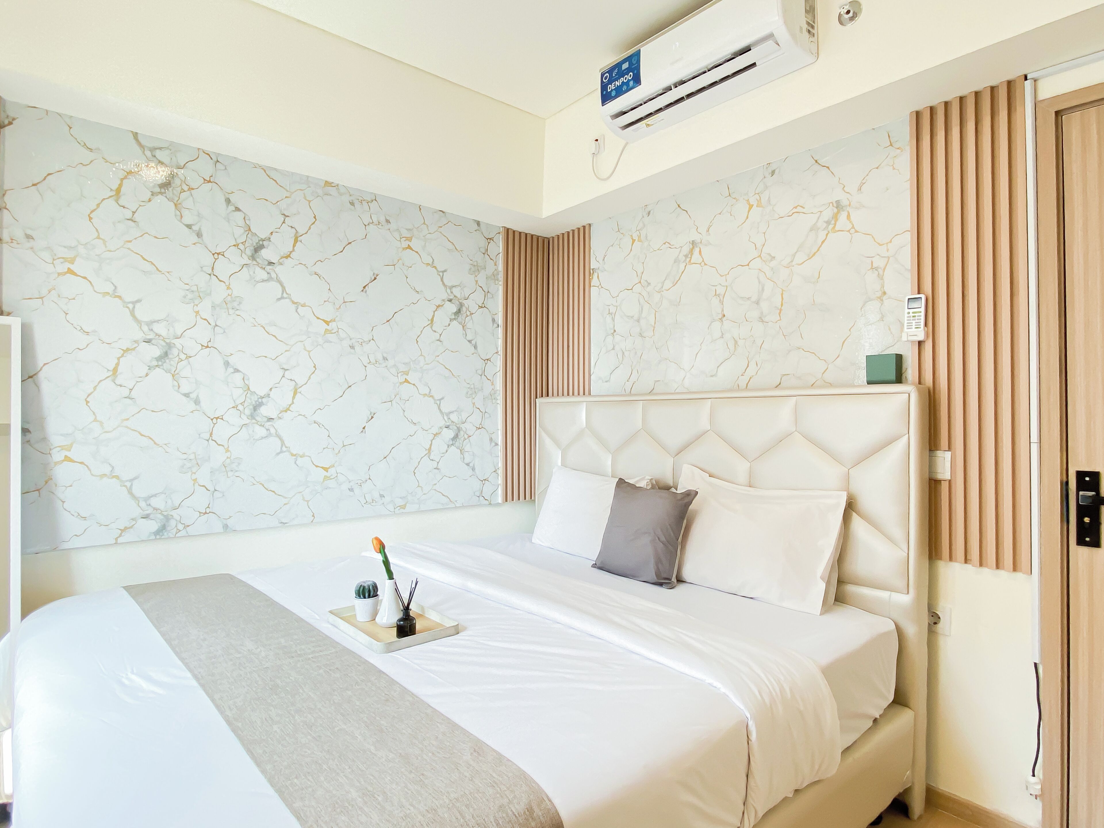 A hotel room with a marble-patterned wall, a bed with a headboard, a bedside table with a tray, and an air conditioning unit.