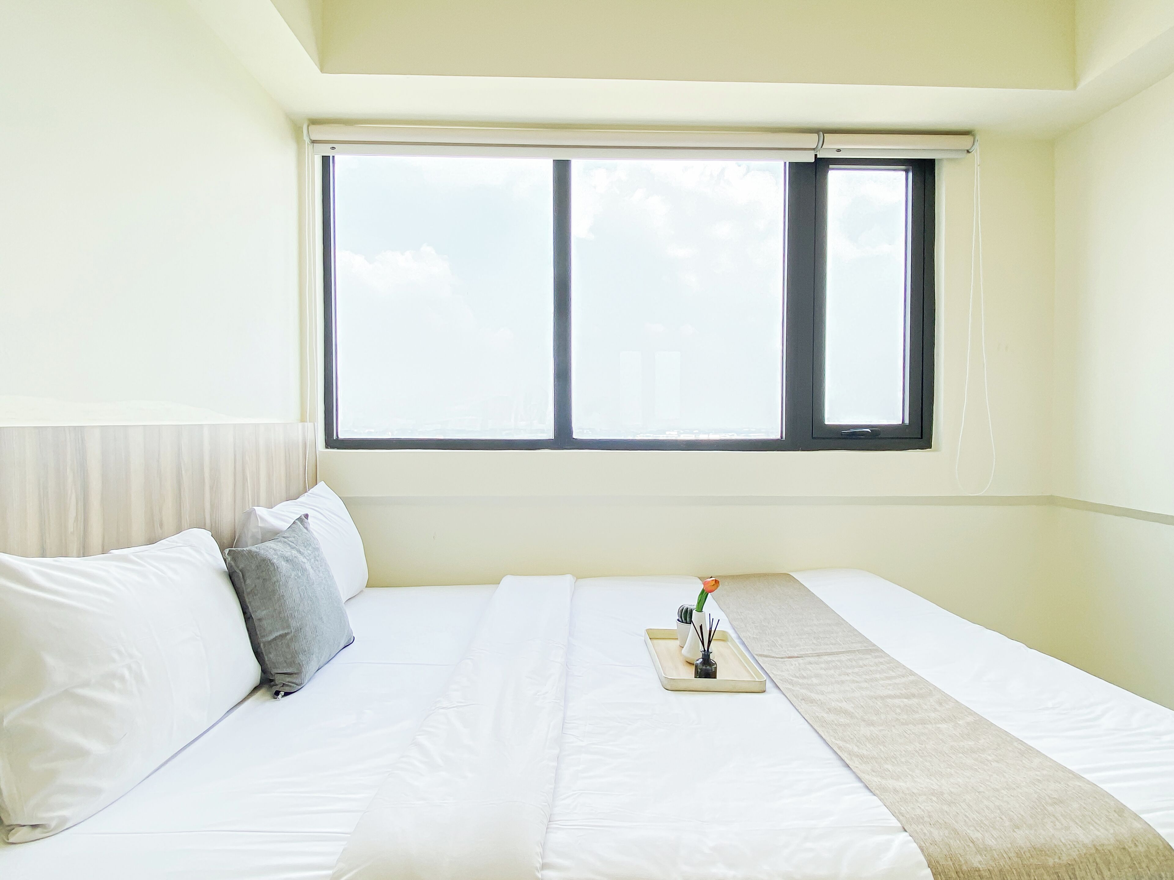 Ein Schlafzimmer mit großem Fenster, einem Bett mit weißer Bettwäsche und einem Nachttisch mit Vase und Tablett.