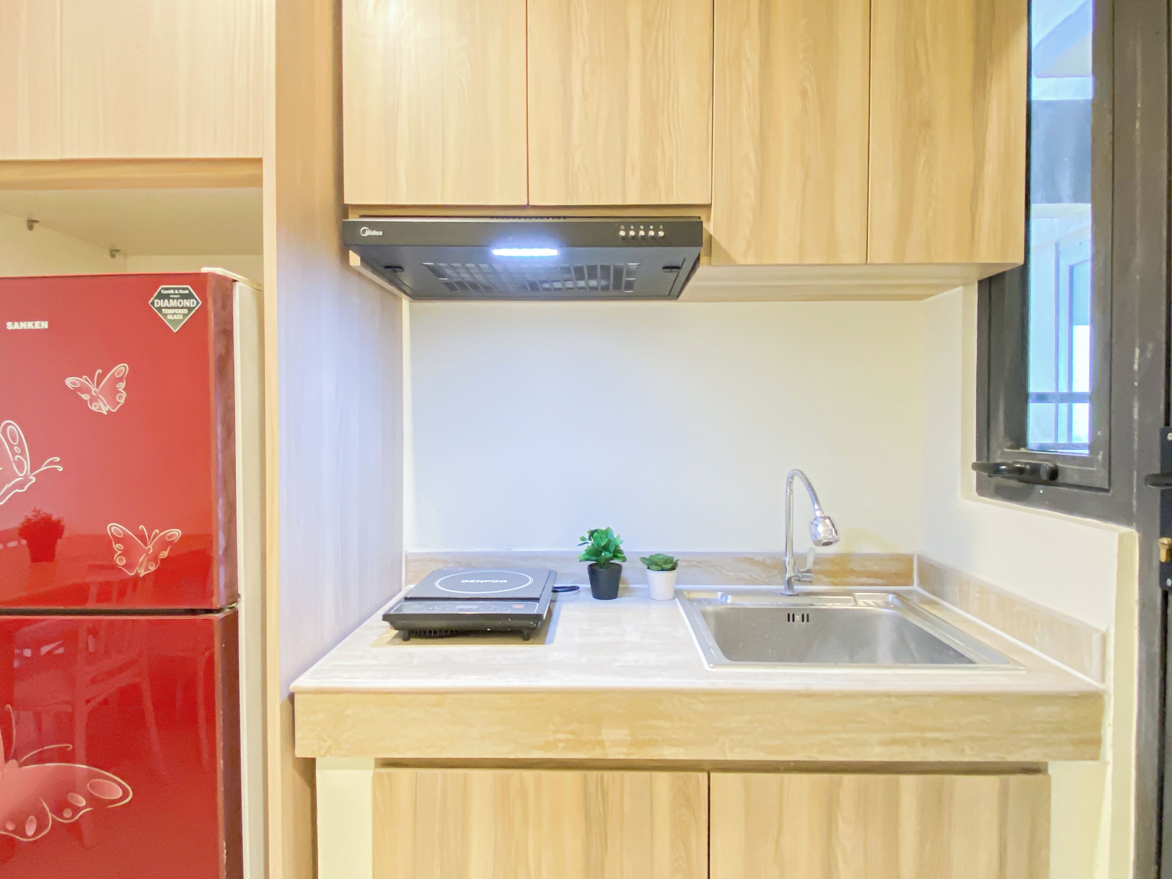 A compact kitchen with a red refrigerator, a built-in stove, a sink, and wooden cabinets.