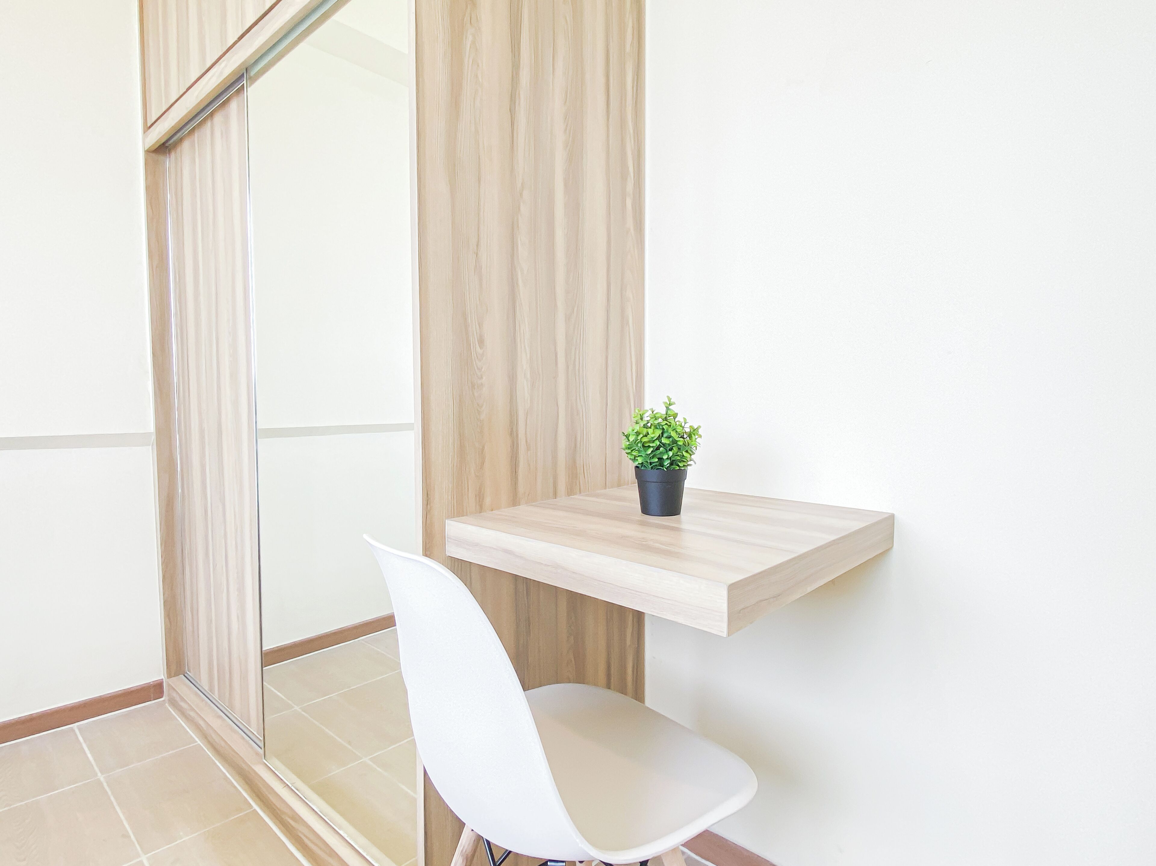 A modern room with a wooden floor, a white chair, a small potted plant on a floating shelf, and a glass partition.