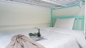 Una cama litera con decoración en blanco y verde azulado, una revista sobre la cama y una planta pequeña.