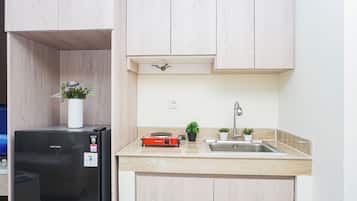 Cocina compacta con refrigerador negro, placa de inducción roja, lavamanos y armarios de madera clara.