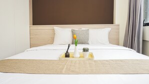 Et hotelværelse med en seng, et natbord med en vase blomster, et bakke med et lys og en lille plante, samt en sengegavl.