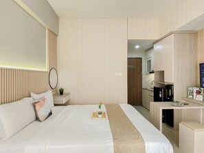 Une chambre d’hôtel comprenant un lit, une table de chevet, une petite plante en pot, un plateau avec une fleur et un coin cuisine.