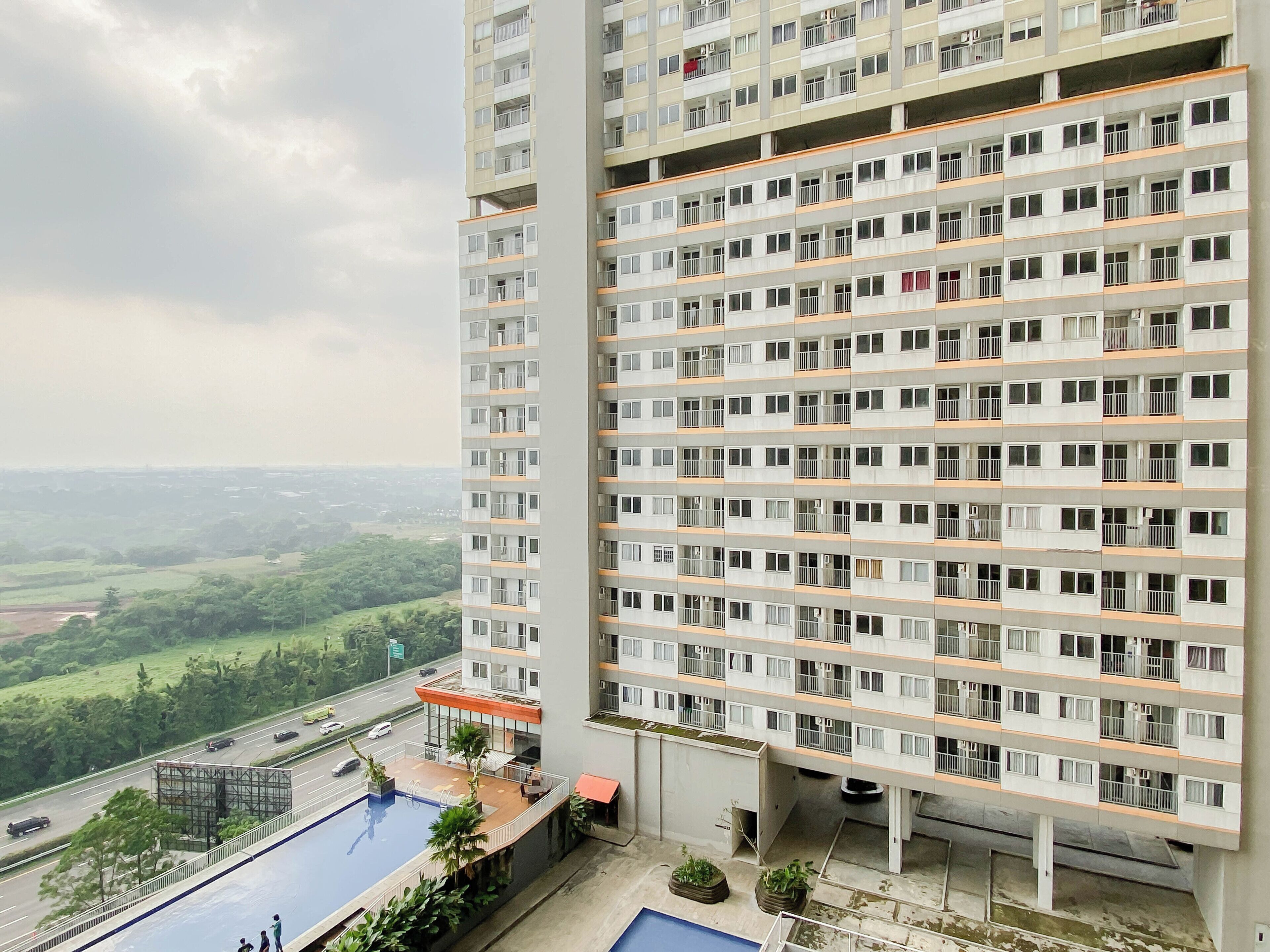 Un edificio de gran altura con varios balcones, una piscina en la azotea y vistas a un paisaje verde.