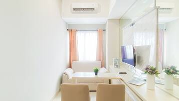 A modern hotel room with a sofa, a desk with a computer, a TV, and a large mirror.