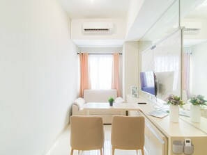 A modern hotel room with a sofa, a desk with a computer, a TV, and a large mirror. - Refined Living 1Br At Apartment Royal Sentul Park (Bogor)