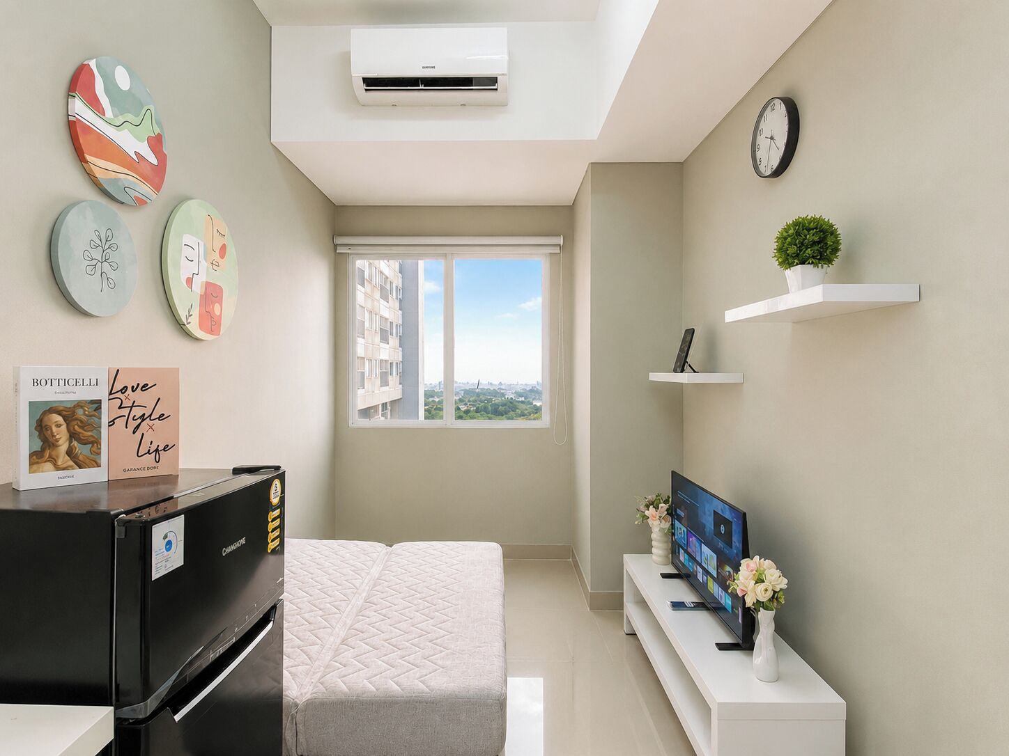 A modern apartment with a bed, a TV, a refrigerator, and a window with a city view.