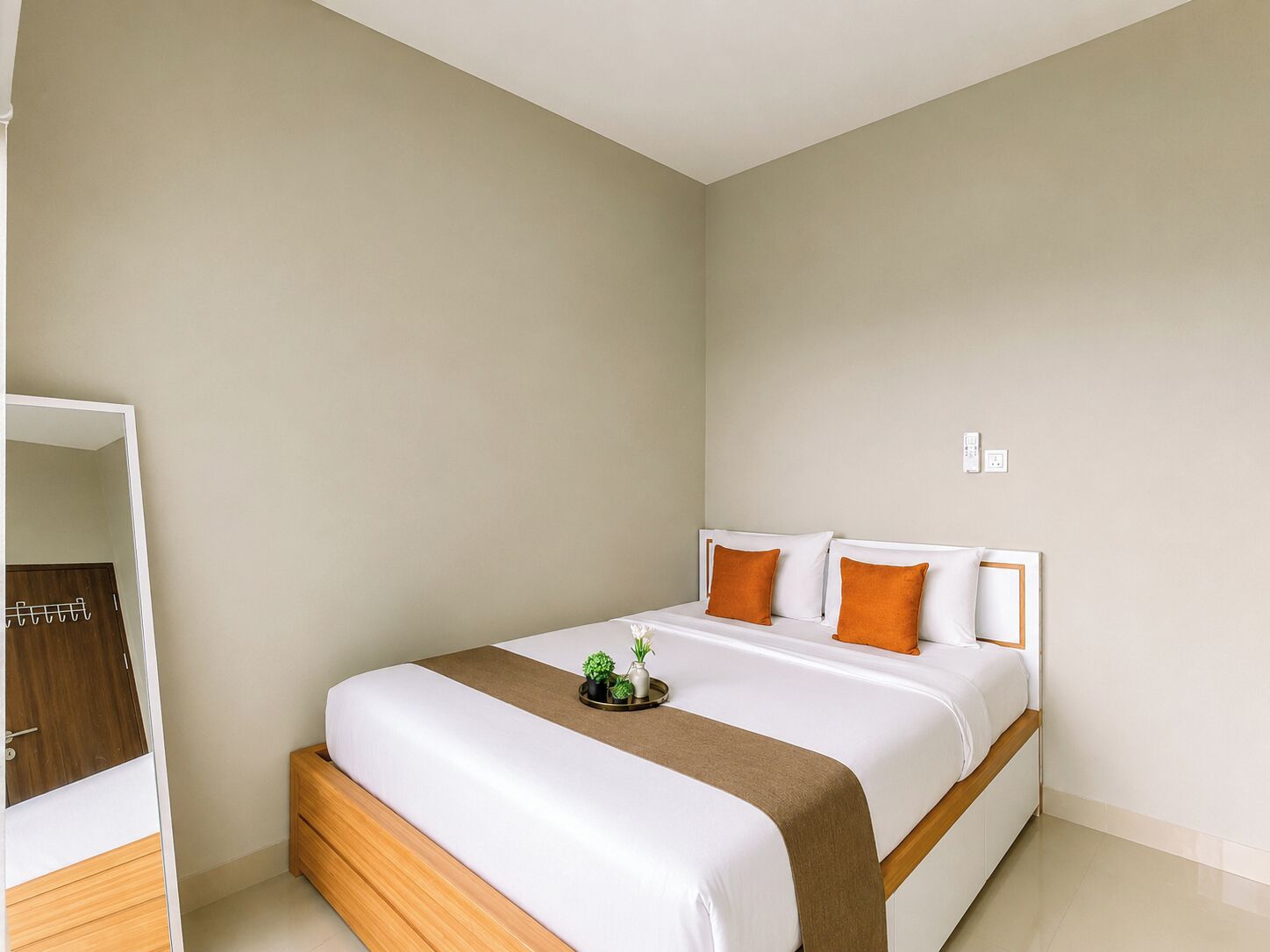 A hotel room with a bed, bedside table, and a small plant.