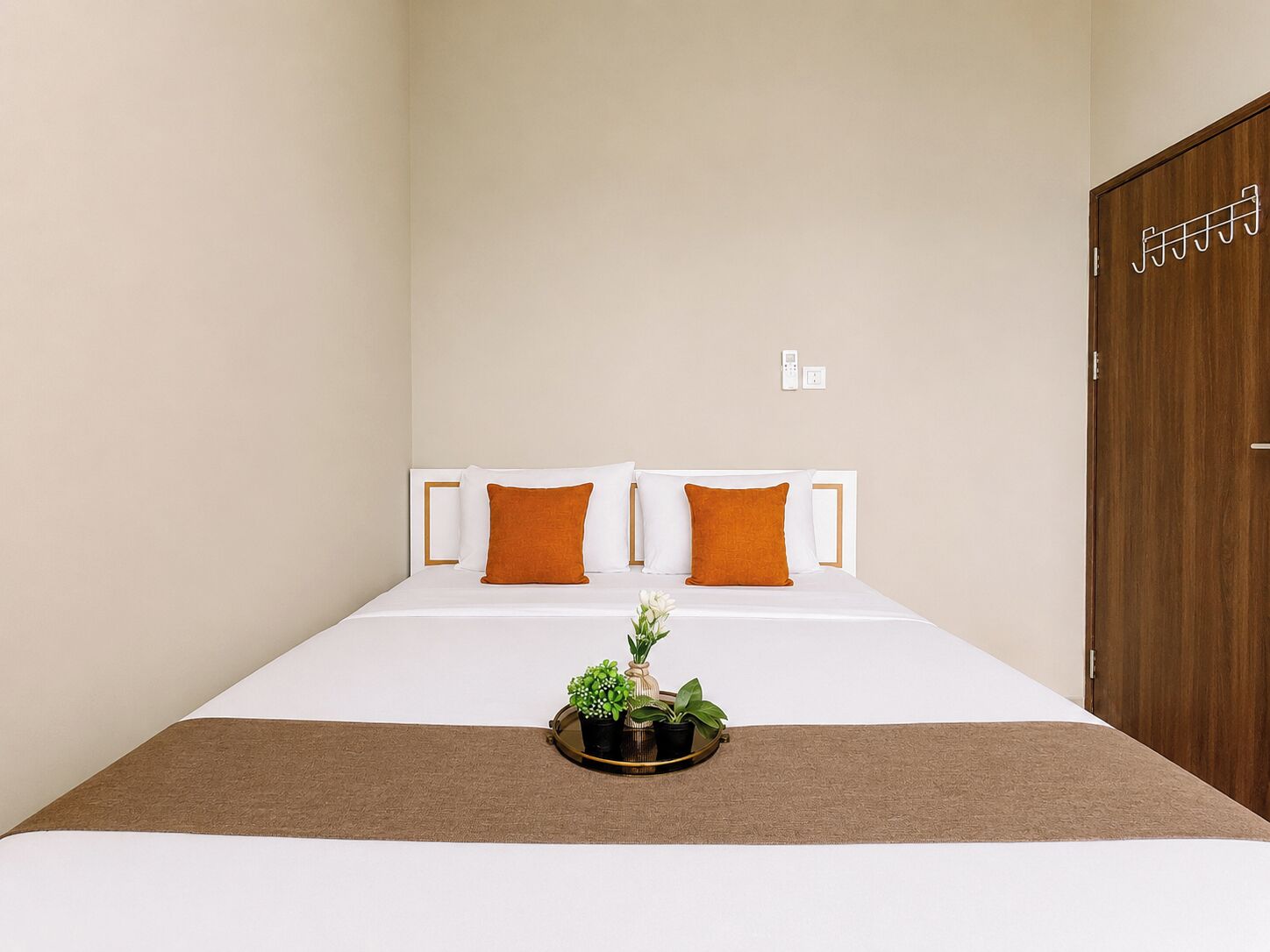 A hotel room with a bed, two pillows, a bedside table with a plant, and a wooden door.