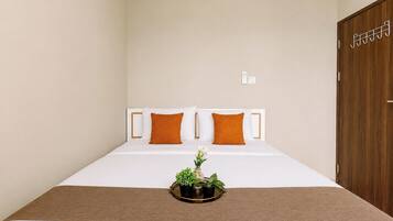 A hotel room with a bed, two pillows, a bedside table with a plant, and a wooden door.