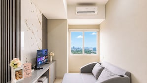 Una camera moderna con un divano grigio, una TV su una scrivania, vista sulla città attraverso una finestra e un condizionatore d'aria.