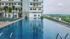 Un edificio moderno con piscina, circondato da palme e vista su zone verdi in lontananza.